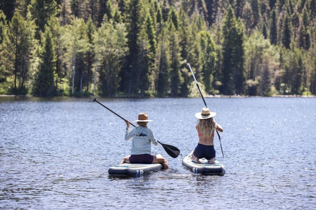 Two women kneeling while paddle boarding on a lake