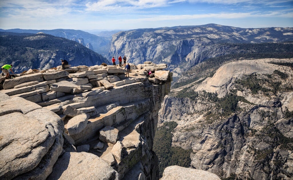 Hikers stand in the distance on top of the summit of Half Dome in Yosemite National Park