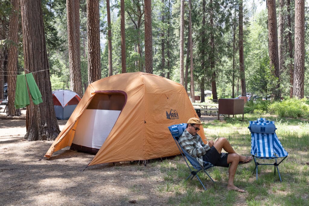 Man writing while sitting in chair in a Yosemite campground with a tent in the background // Yosemite camping and lodging is included in this Yosemite National Park guide