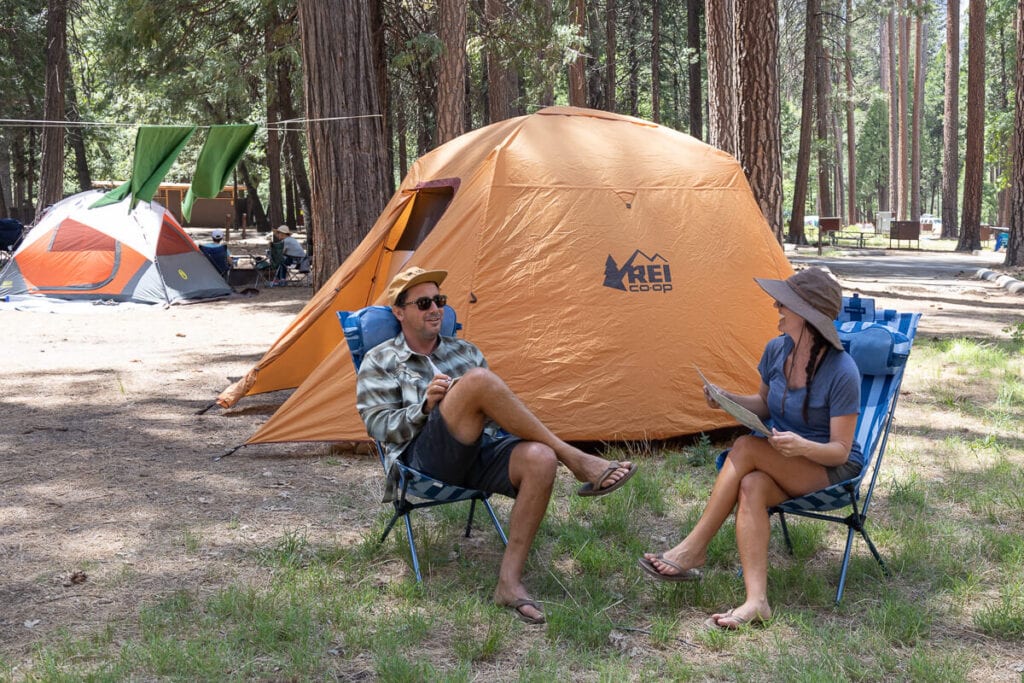 Two people sitting in camping chairs at campground with tents set up around them