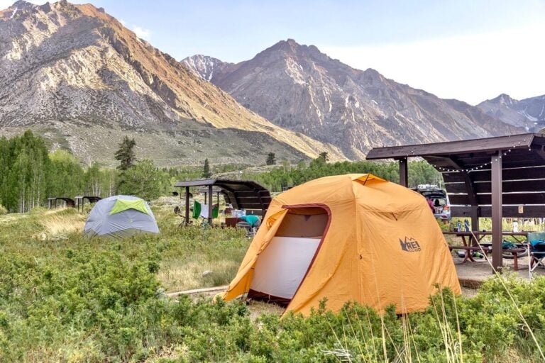 An orange tent at a campsite with green grass and mountains