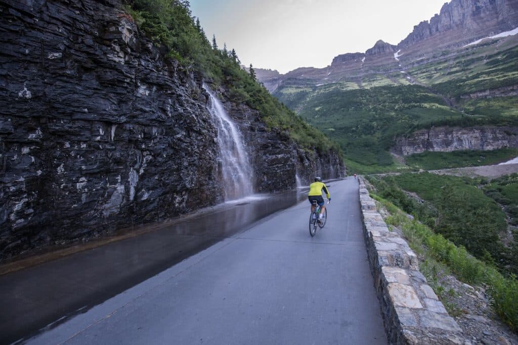 Cyclist passing a waterfall on the scenic Going to the Sun Road in Glacier National Park