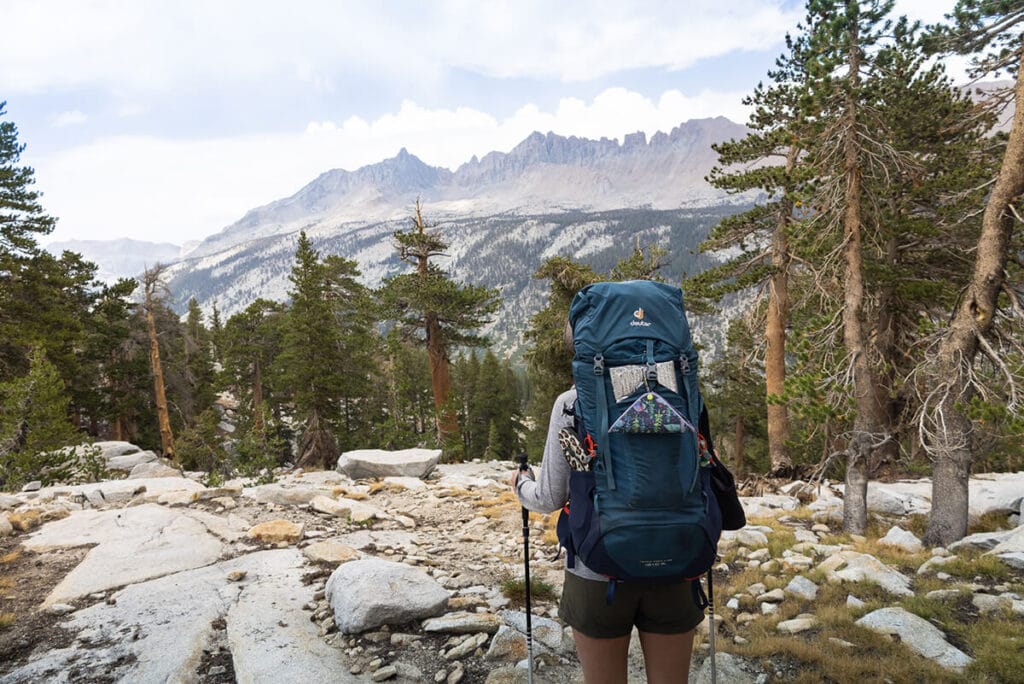 A woman from behind backpacking in Sequoia National Park. She's wearing a blue backpacking pack with a Kula Cloth hanging off the side