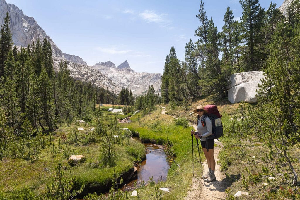 A woman stands on a hiking trail next to a small stream in Sequoia National Park