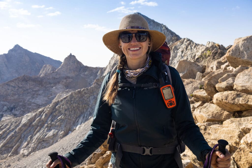 a woman smiling wearing Arc'teryx SL Insulated Hoodie with mountains in the background and a backpacking pack