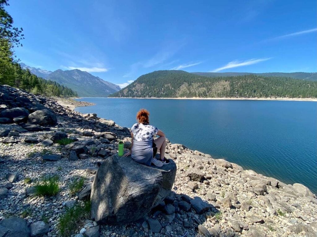 Woman hiker sitting on rock at lake shore facing away from camera