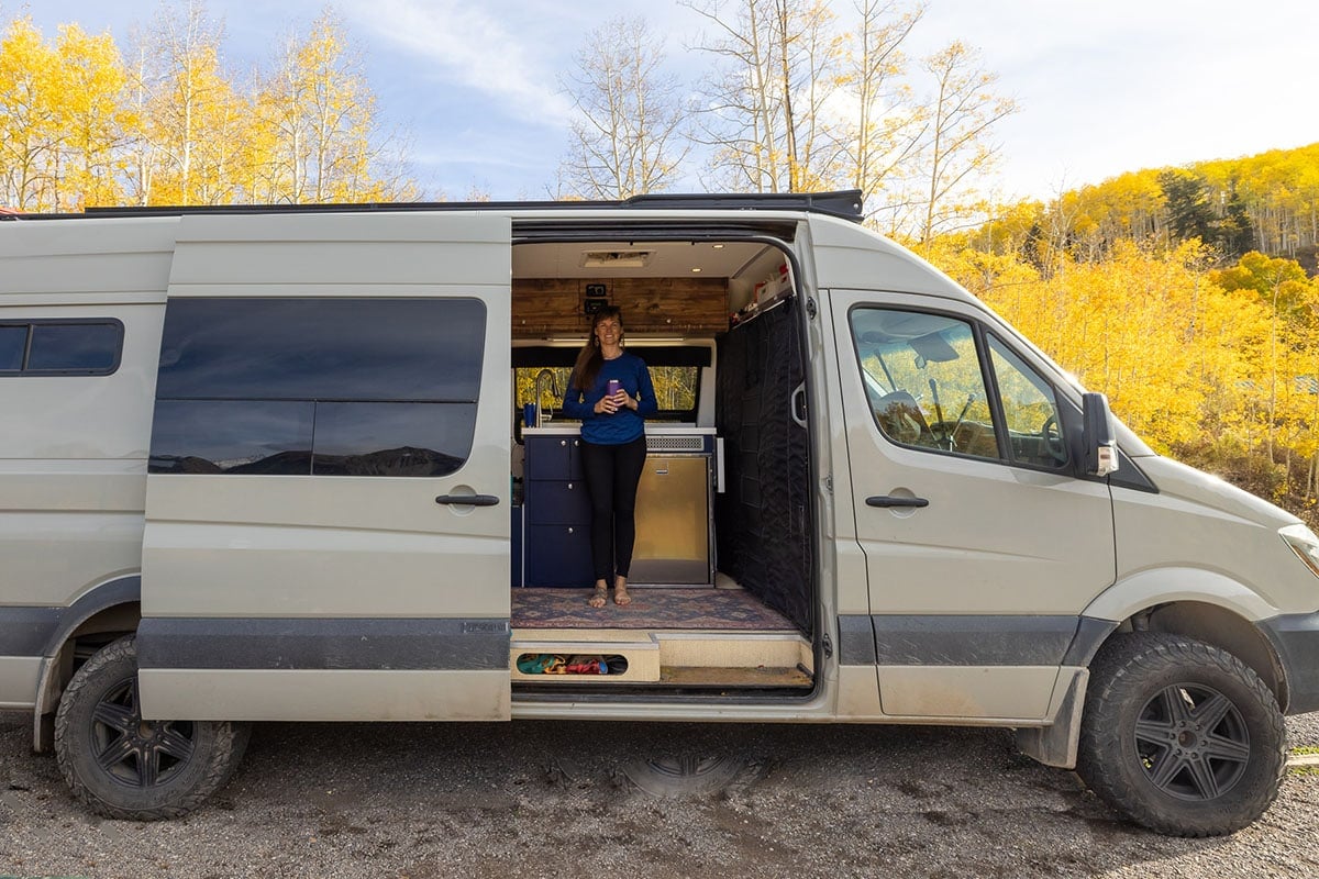 Bearfoot Theory founder Kristen Bor standing in the doorway of a Sprinter camper van in Telluride Colorado with golden aspens behind the van