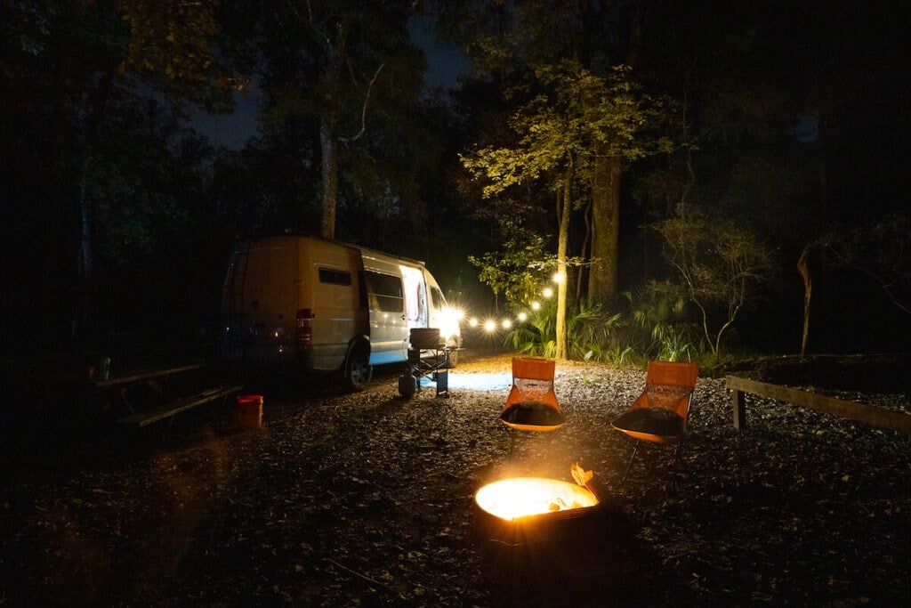 Sprinter Van camping with a bonfire, string lights, and camp chairs