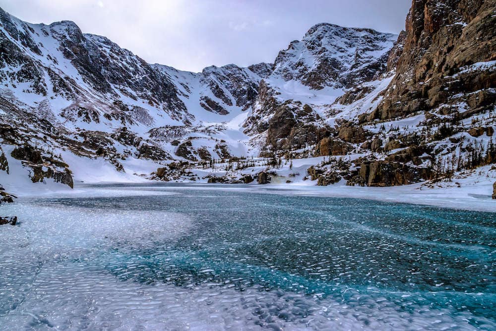 Frozen over blue lake in Rocky Mountain National Park surrounded by snowy mountains