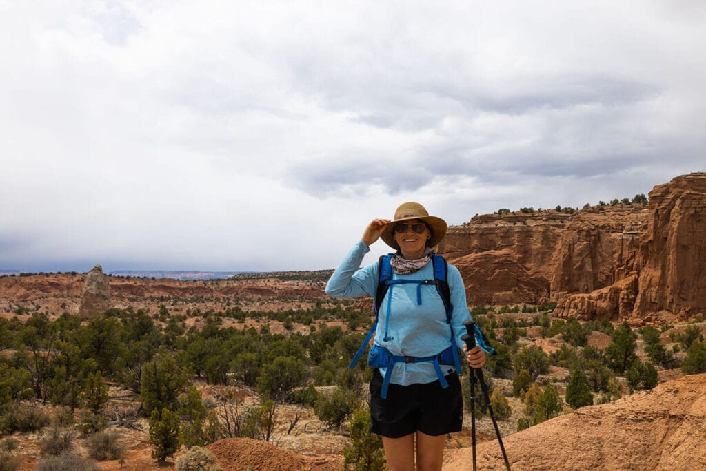 Kristen dressed in hiking gear and holding trekking poles on trail in Kodachrome Basin in Utah with red rock landscape behind her