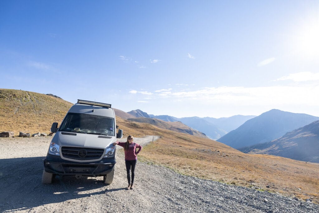 Kristen standing next to van parked on side of dirt road winding through mountain pass in Colorado