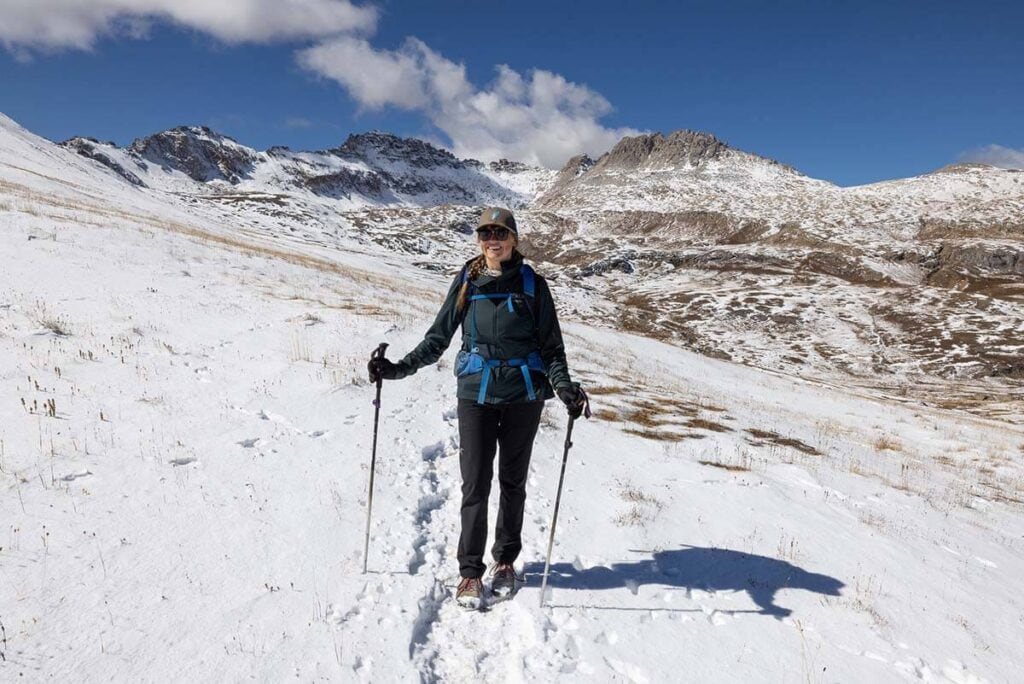 Kristen on snowy hiking trail in Colorado with trekking poles and wearing winter hiking clothes