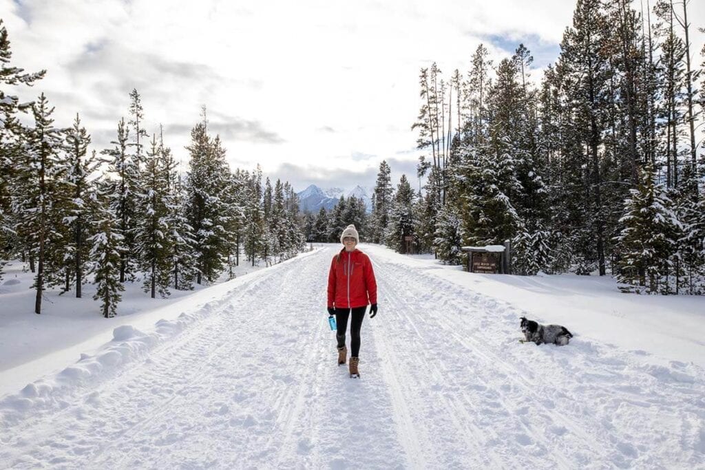 Woman wearing bright red jacket walking on snowy track with dog