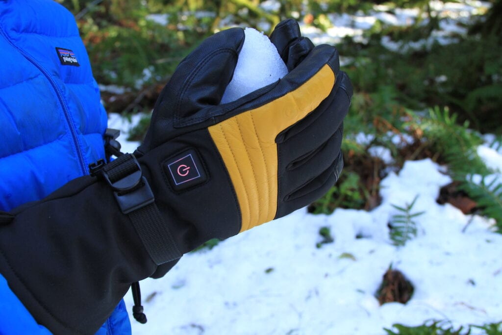 Gobi Heat Vertex Heated Glove // person holding a snowball outside wearing a blue jacket and black and yellow heated gloves