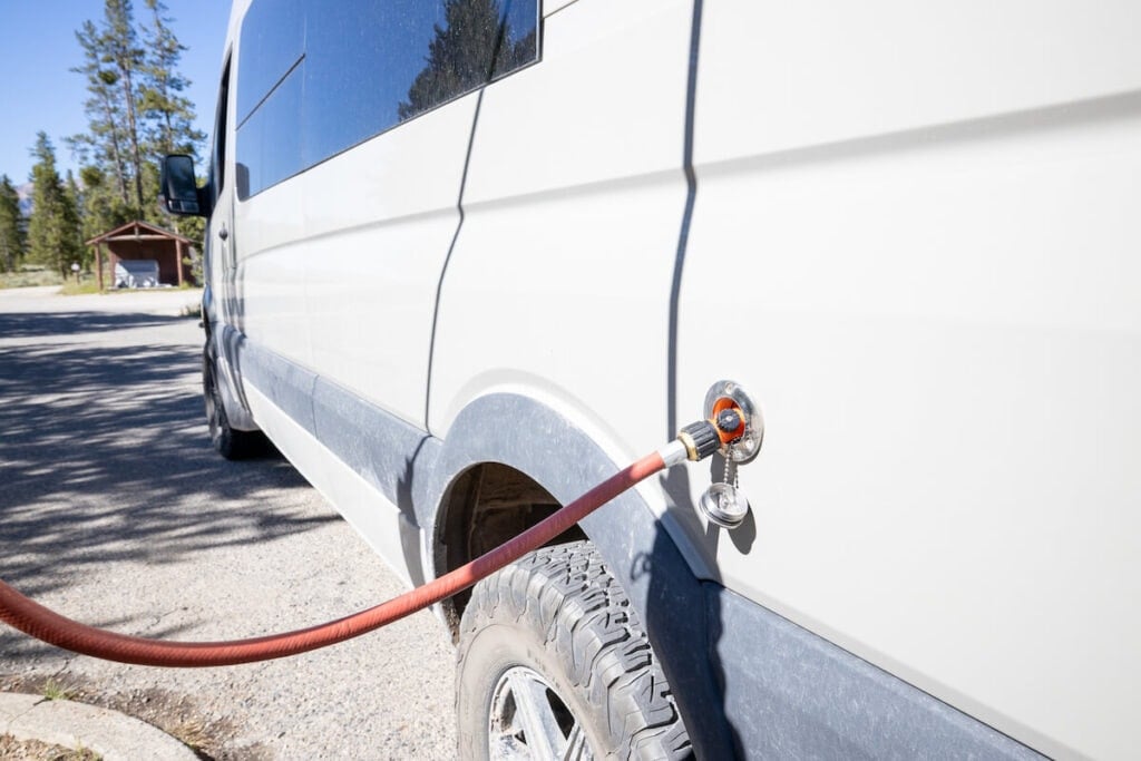 a fill port on the outside of a Sprinter campervan with a red hose attached to refill water at a dump station