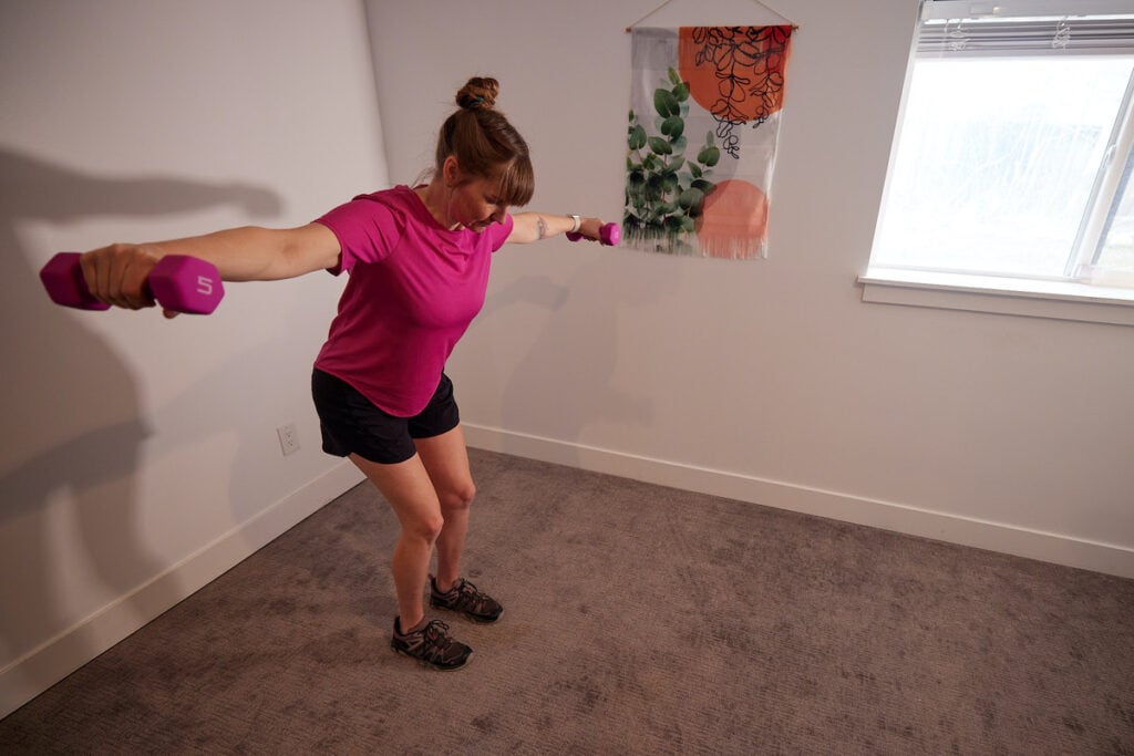 Woman exercising with light weights at home in the lululemon High Neck Run and Train Tee