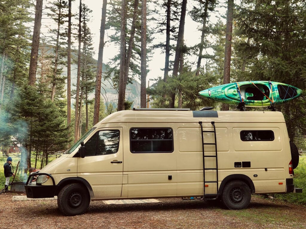 Tan Sprinter camper van in a forested campground available for rent through Tierra Traveler