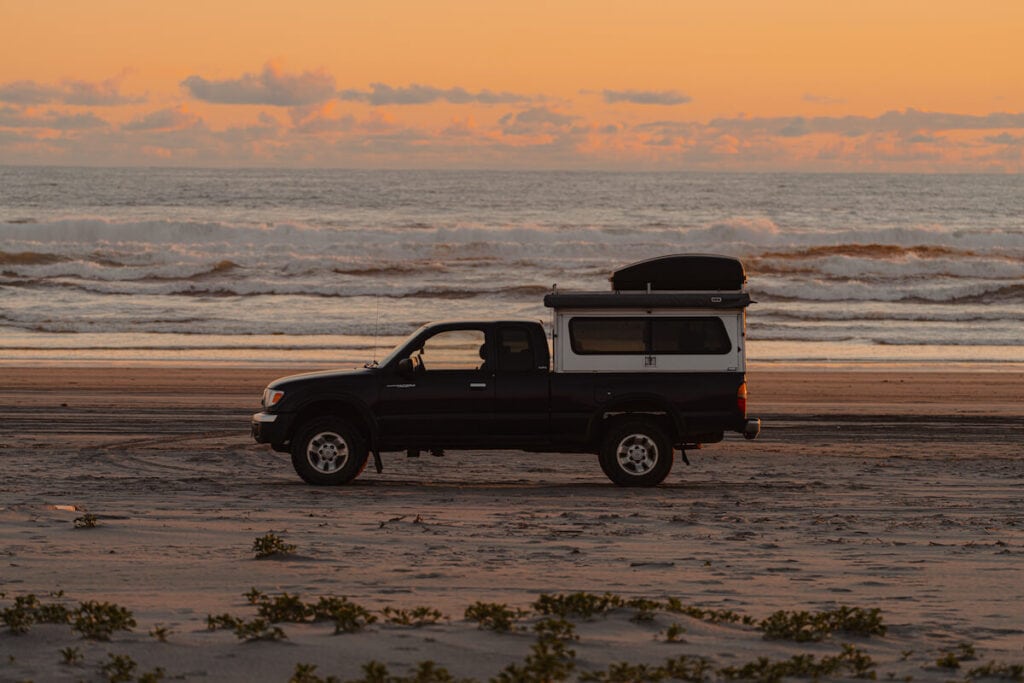 a truck camper on a beach at sunset