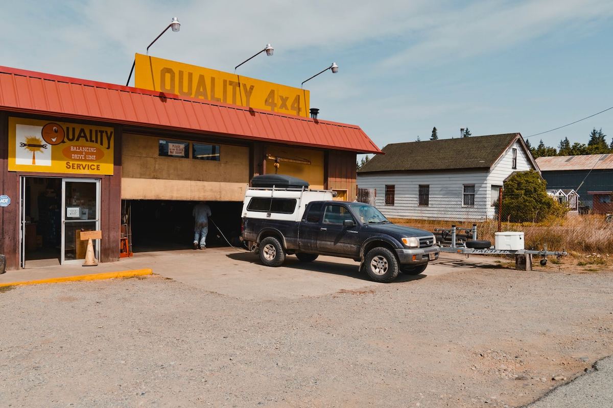 Pickup truck with camper parked in front of mechanic shop with yellow sign that says 