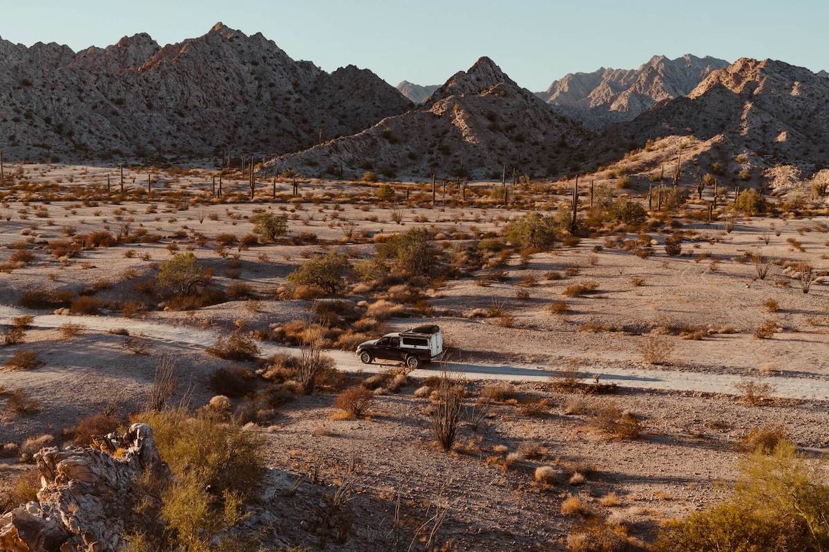 Pickup truck with camper on remote dirt road is the desert with rocky mountains in the background