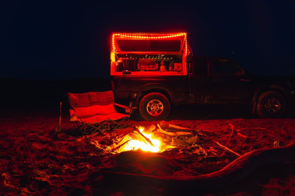 Campsite lit up by fire with double camp chair and truck camper nearby