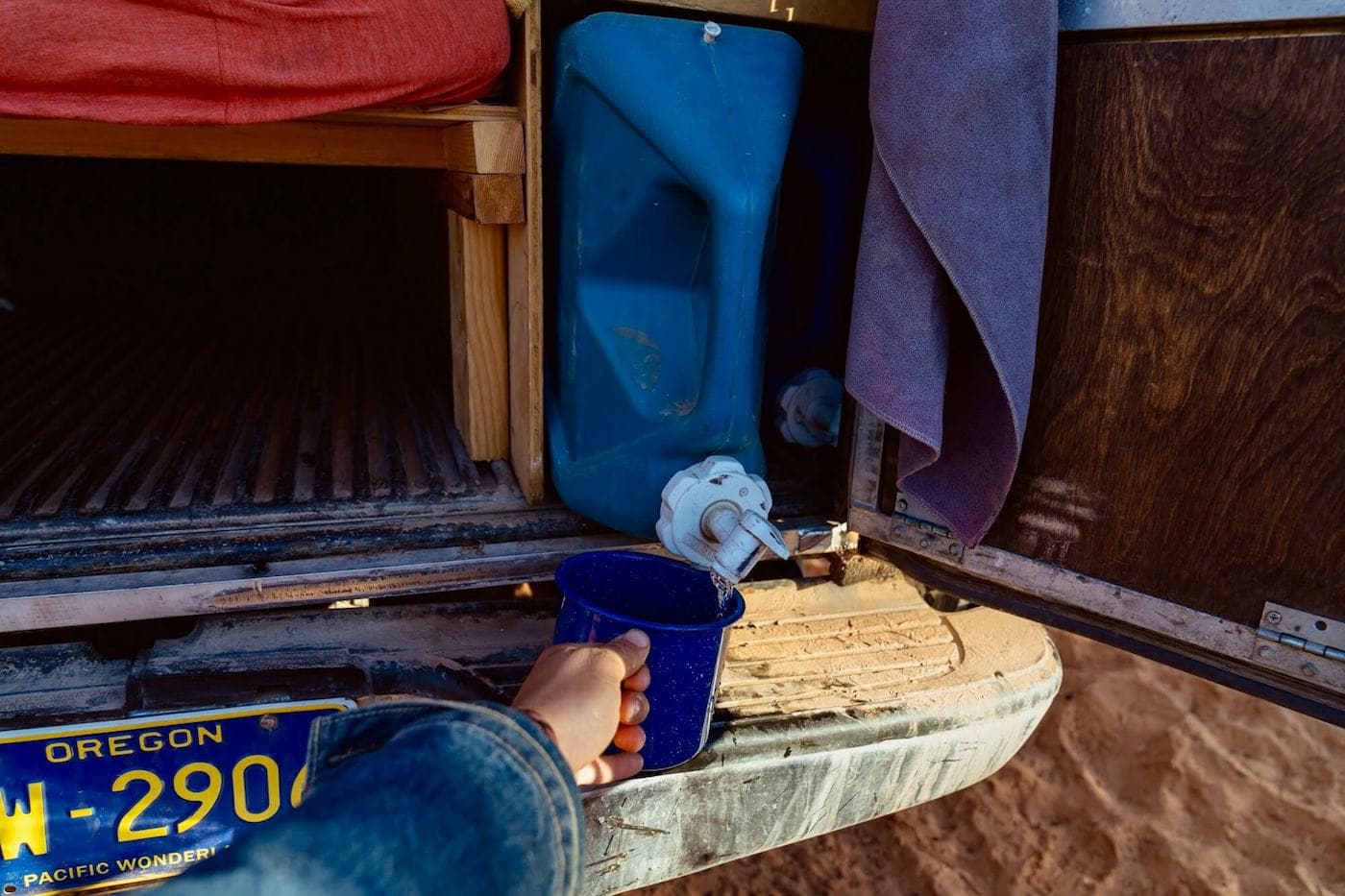 Person filling cup from blue water jug in back of truck camper