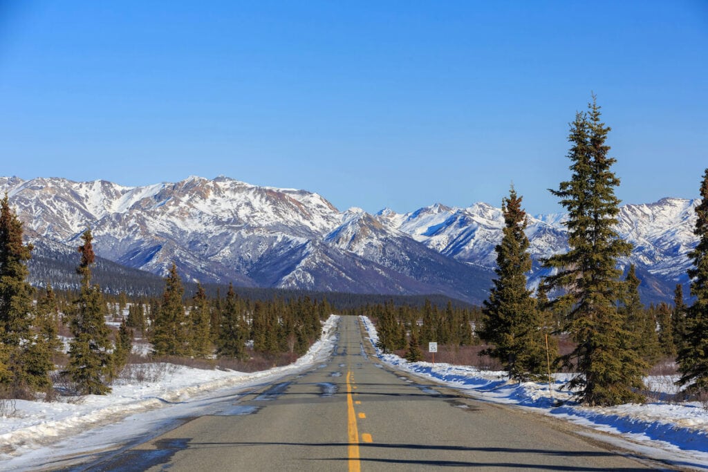 an icy road in Alaska in winter with snow capped mountains in the distance