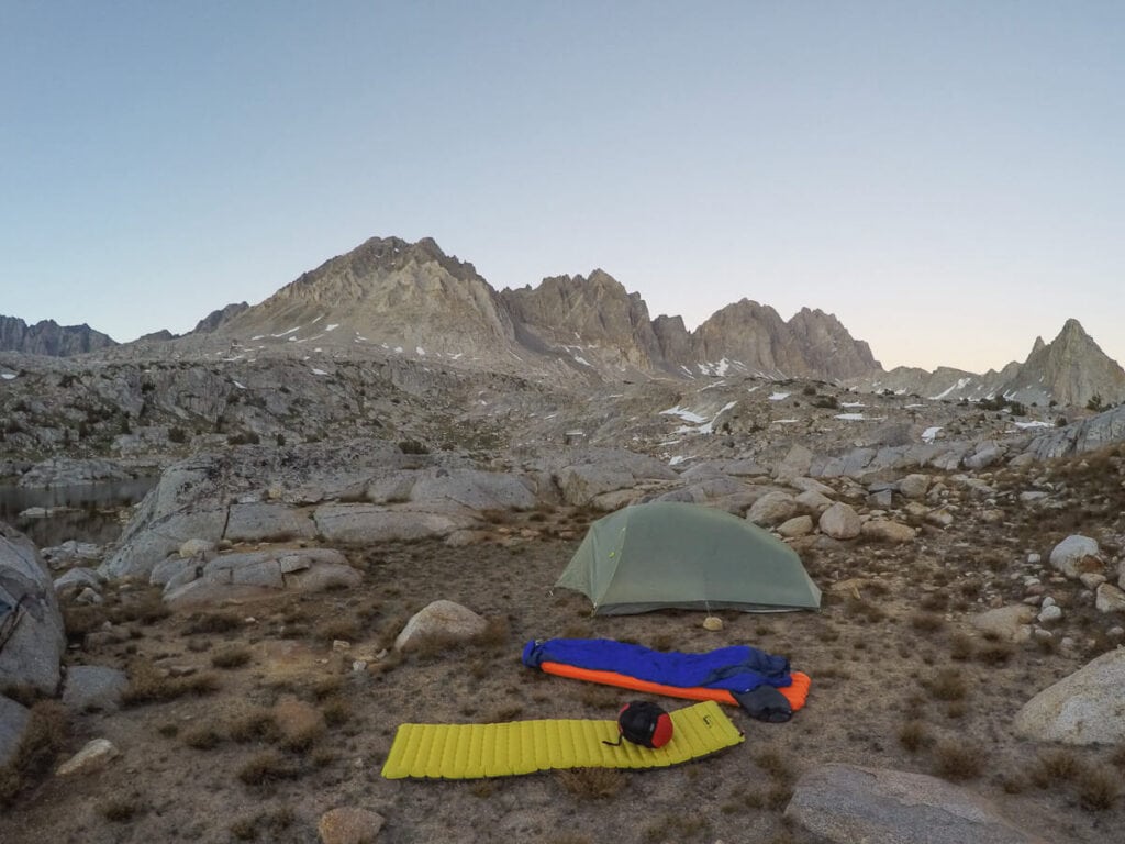 a yellow sleeping pad outside of a backpacking tent next to a sleeping bag in the mountains