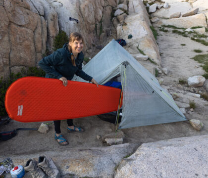 a woman holding a red therm-a-rest prolite plus sleeping pad and putting it into her backpacking tent