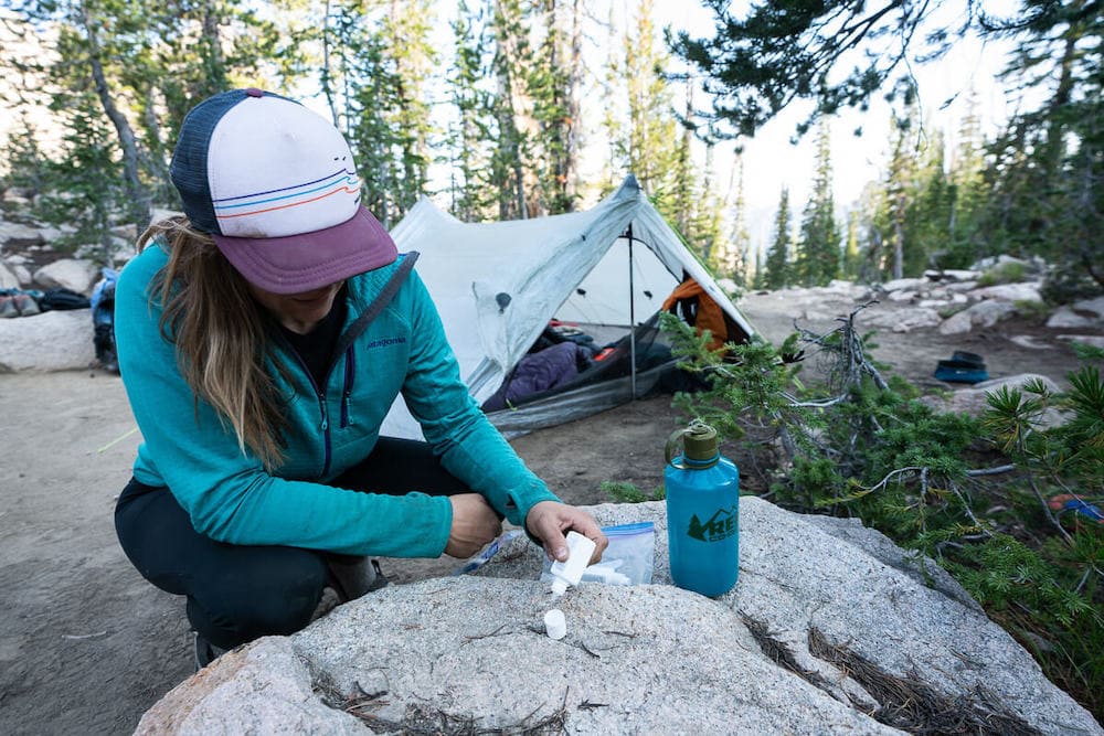 Woman preparing water purification drops at backcountry campsite