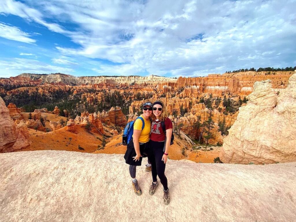 Two women posing for photo at scenic overlook in Bryce Canyon National Park with hoodoo rock formations in background