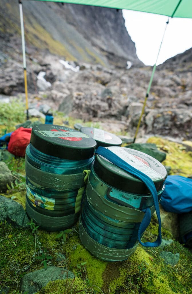 Two packed BearVault BV 500 bear canisters on ground under tarp in Alaska