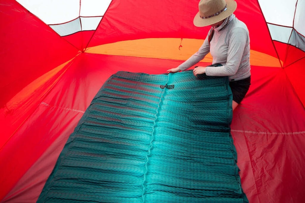 A woman holds up the deflated NEMO Roamer Double Sleeping Pad to begin to roll it up