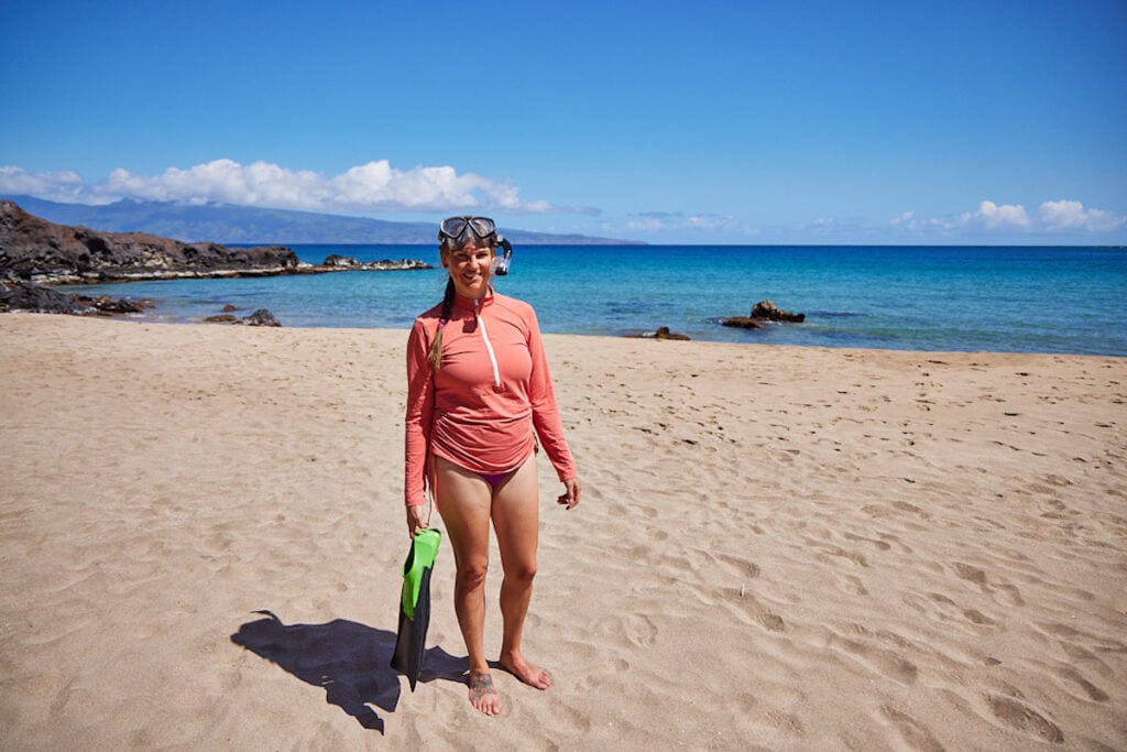 A woman holds fins while wearing the Carve Designs Cruz rashguard on a beach in Maui