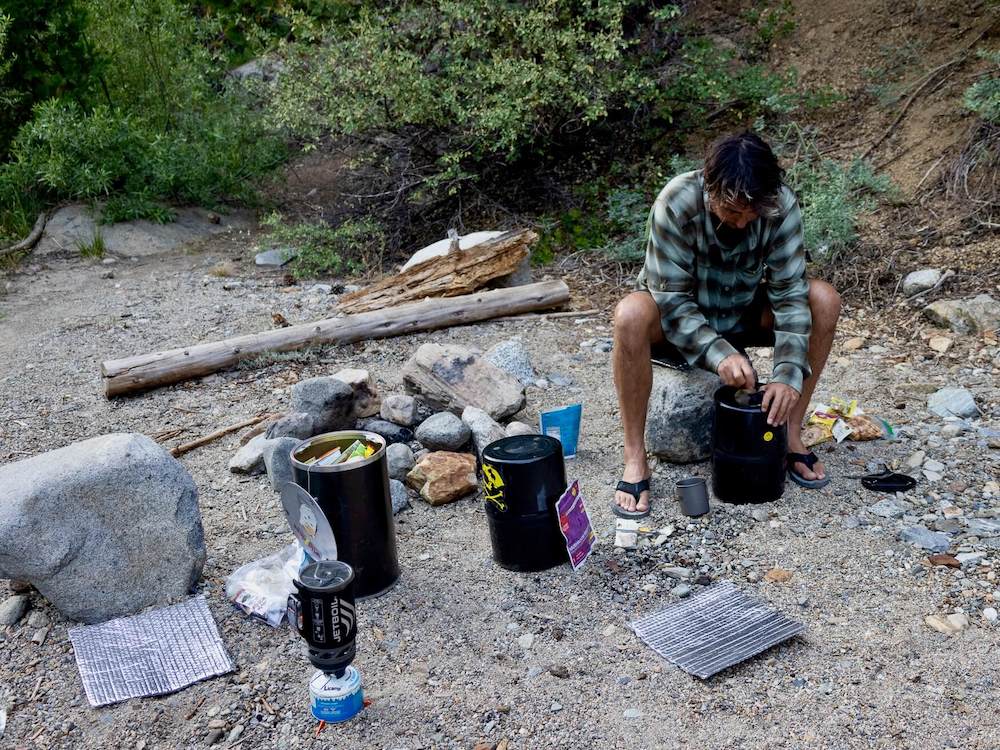 Backpacker sitting on rock at camp taking food out of bear canister