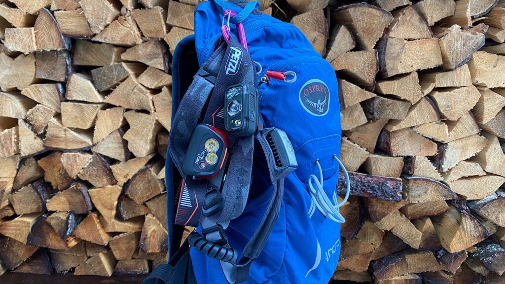 Three headlamps hanging on the side of a blue daypack