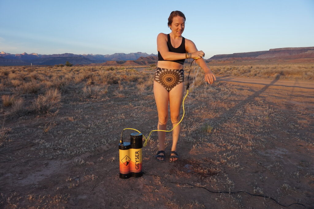 A woman rinses off using the geyser systems portable shower system. she is in the desert of southern utah.