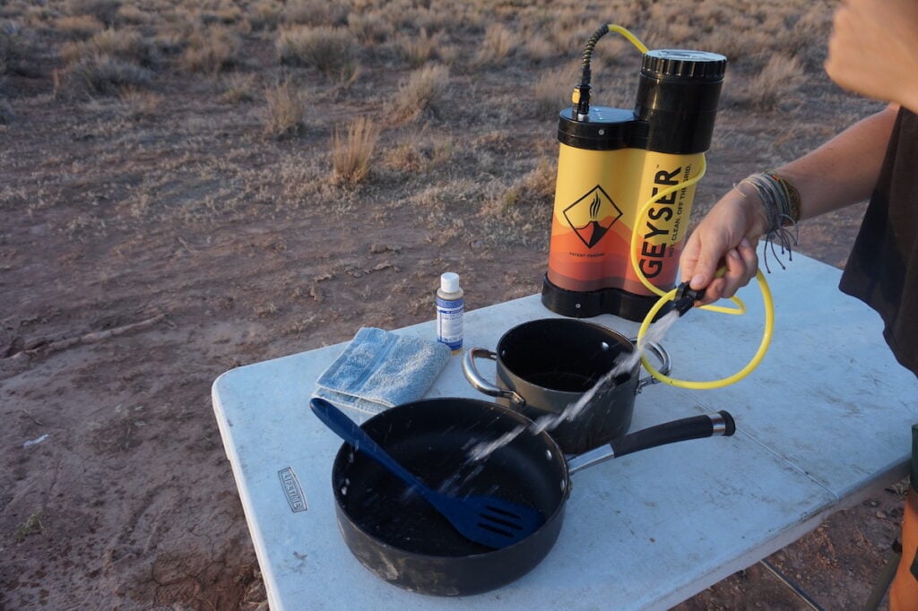 A woman washes dishes using the Geyser Systems Portable Shower With Heater