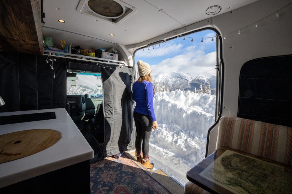 Woman standing in door of open converted Sprinter van looking out into snowy landscape