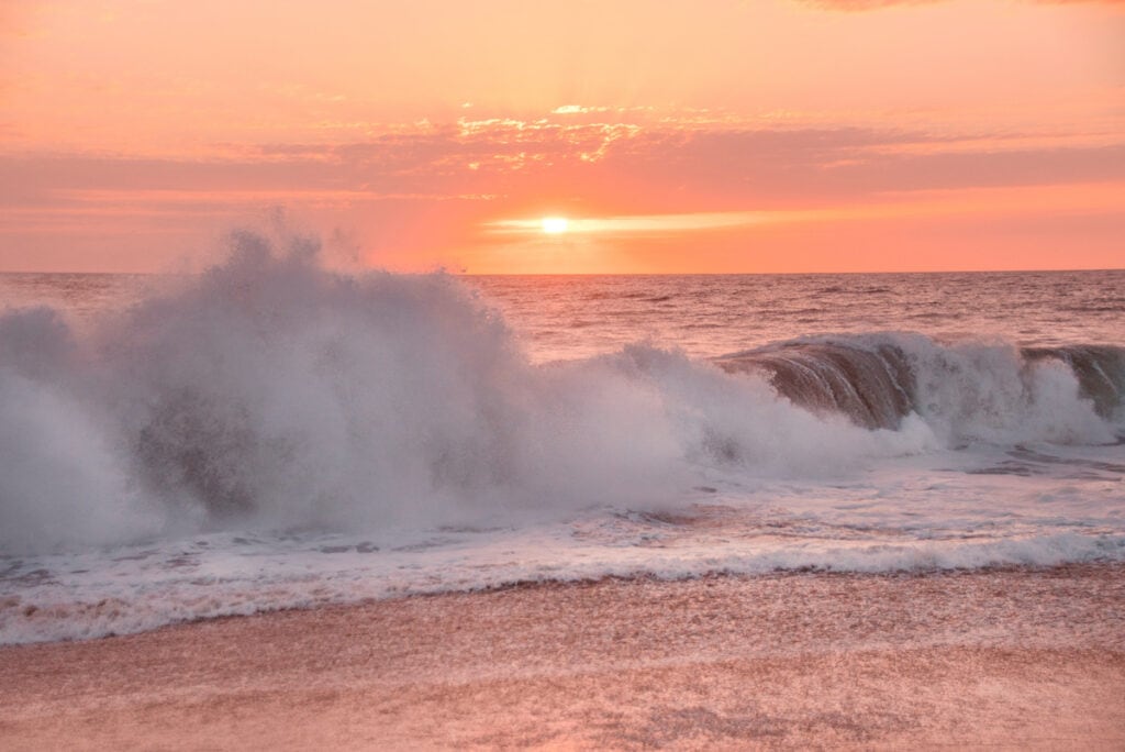 A pink sunset on a beach in Todos Santos with waves crashing on the shore