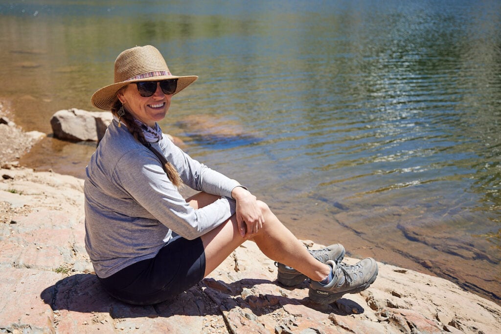 A woman sitting next to a lake wearing Oboz Sawtooth X hiking boots