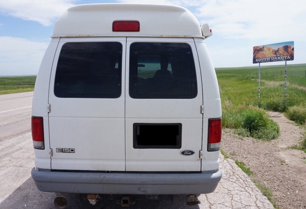 a white Ford E150 van parked next to the "Welcome to South Dakota" sign