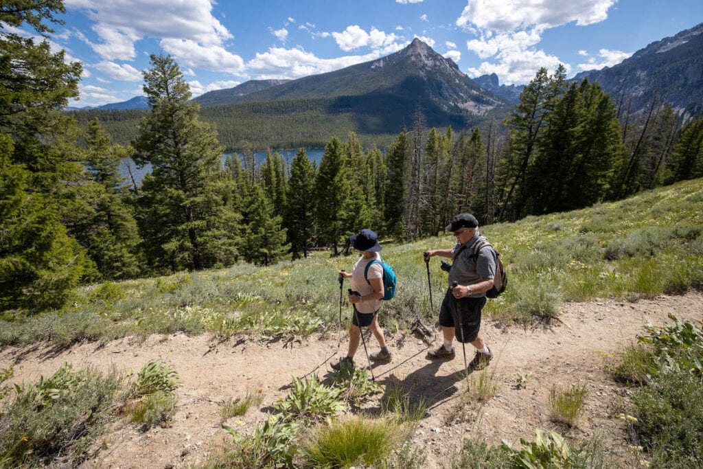 Two senior hikers on trail in Idaho with mountains and lake in background