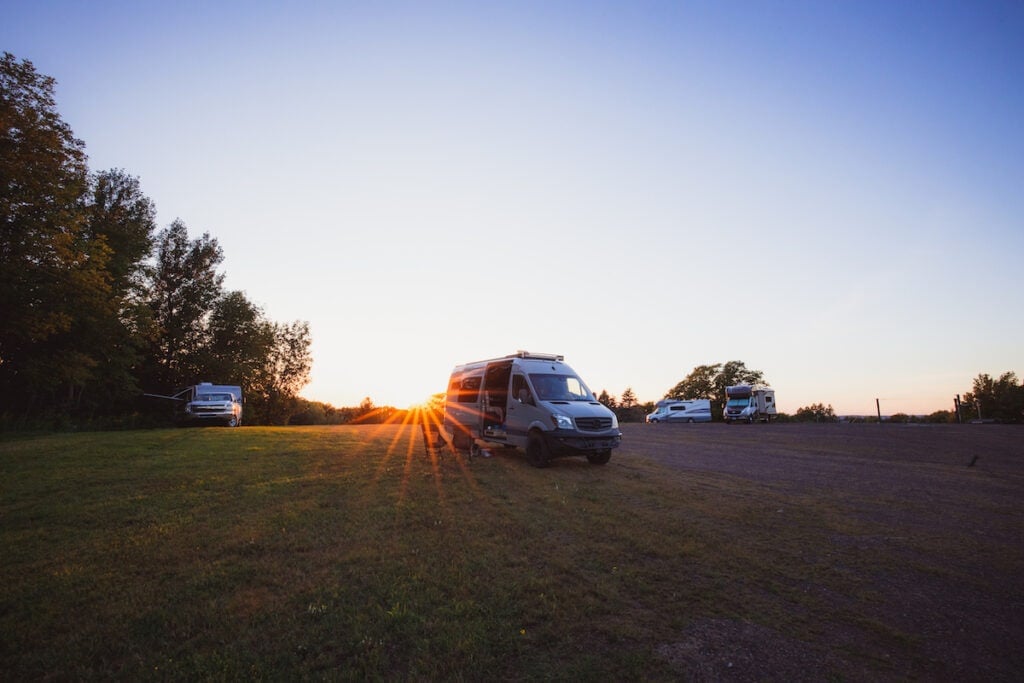 Algumas vans estão estacionadas em um campo ao pôr do sol.  Eles estão acampados em um local da Harvest Hosts em Michigan.