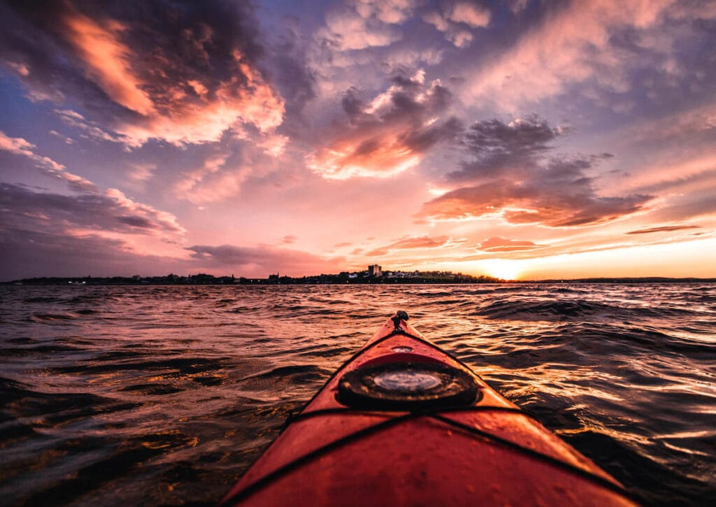 View out over front of kayak with Portland Maine skyline in distance and sunset skies overhead