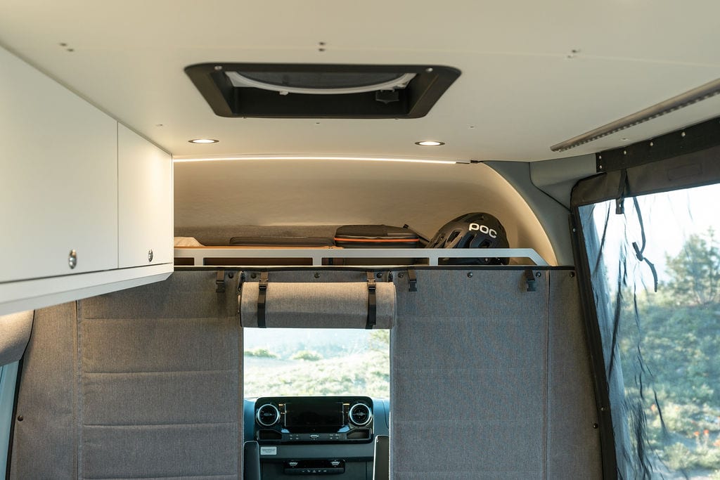 Over cab storage and a insulating curtain in a Sprinter Van conversion built by Outside Van