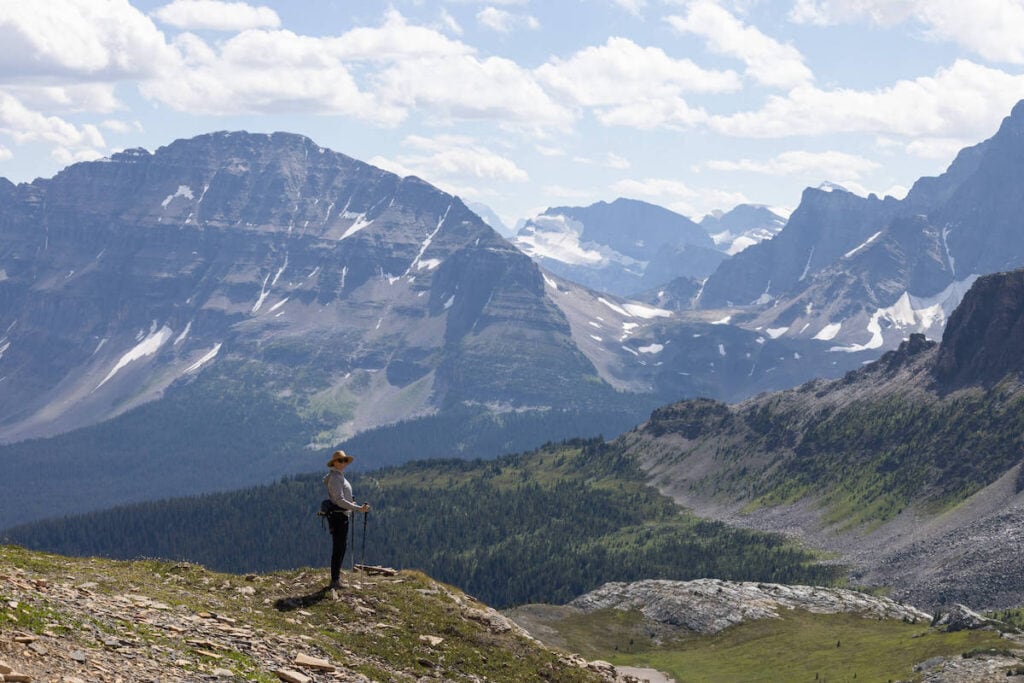 Woman hiker standing at overlook with jagged Rocky Mountains and snow patches in background on Helen Lake Trail on Icefields Parkway in Alberta Canada