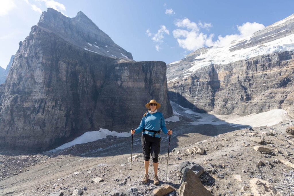 Alpinista feminina parada em uma trilha perto de Lake Louise, BC, para foto com picos áridos, rochosos e cobertos de neve como pano de fundo