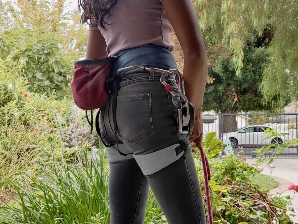 Woman modeling rock climbing gear including a harness, chalk bag, carabiners, and rope