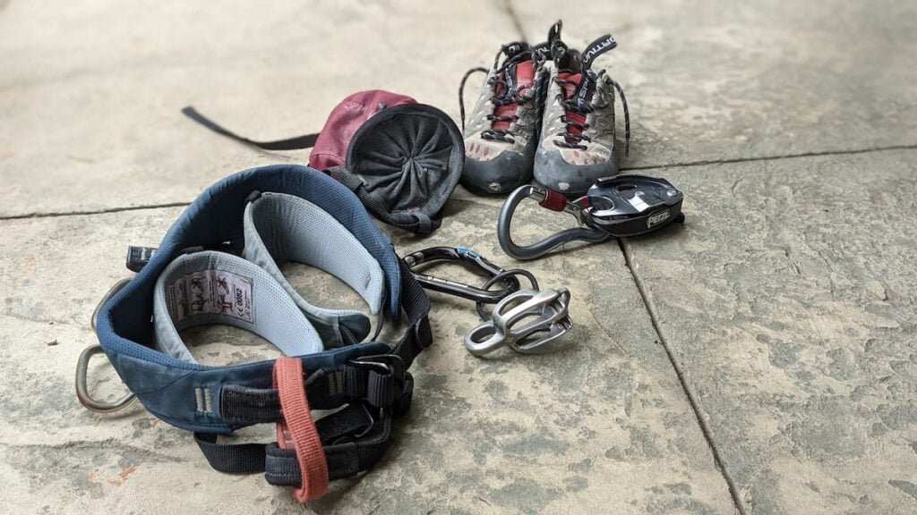 A close up of what to bring indoor rocking climbing: a harness, chalk bag, climbing shoes, and belay device